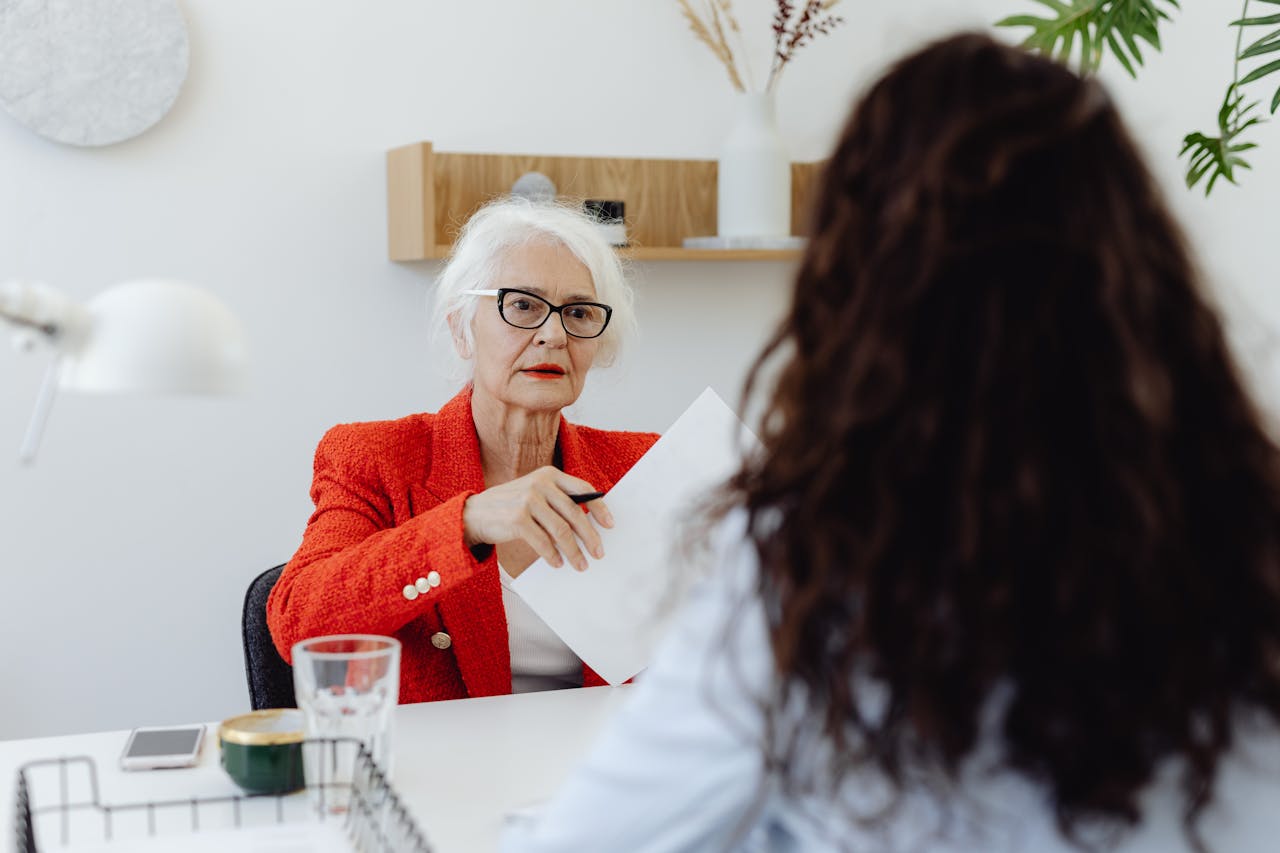 Senior businesswoman in red blazer engaging in a document review meeting in a modern office setting.